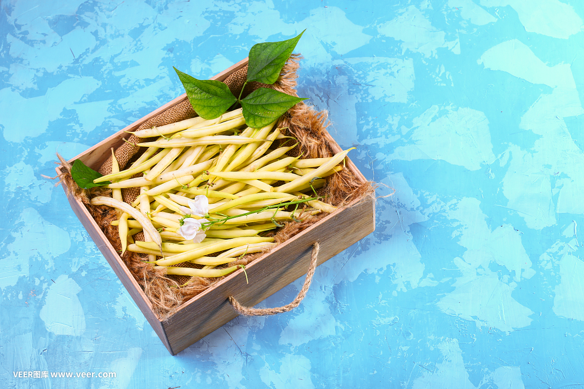 黄色的豆子,农场新鲜蔬菜和有机产品在一个木盒子-新鲜的豆子在蓝色的背景。俯视图拷贝空间